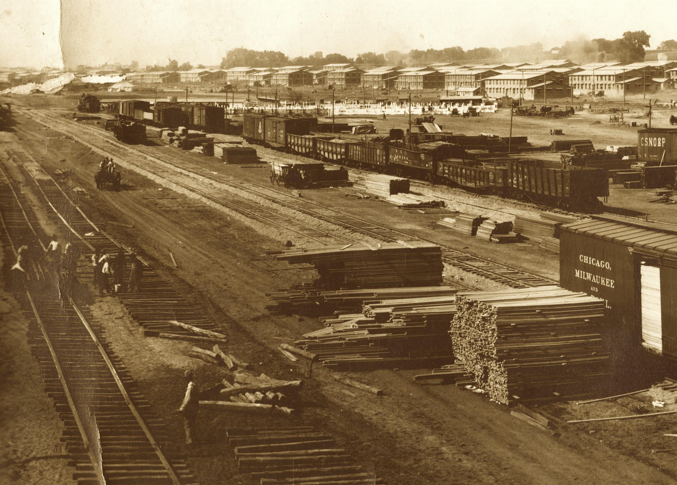 Stacked lumber unloaded from railcars at Camp Dodge awaits transport by horse drawn wagons as workers prepare additional rail riding sidings in late summer 1917. Photo courtesy of Iowa Gold Star Military Museum